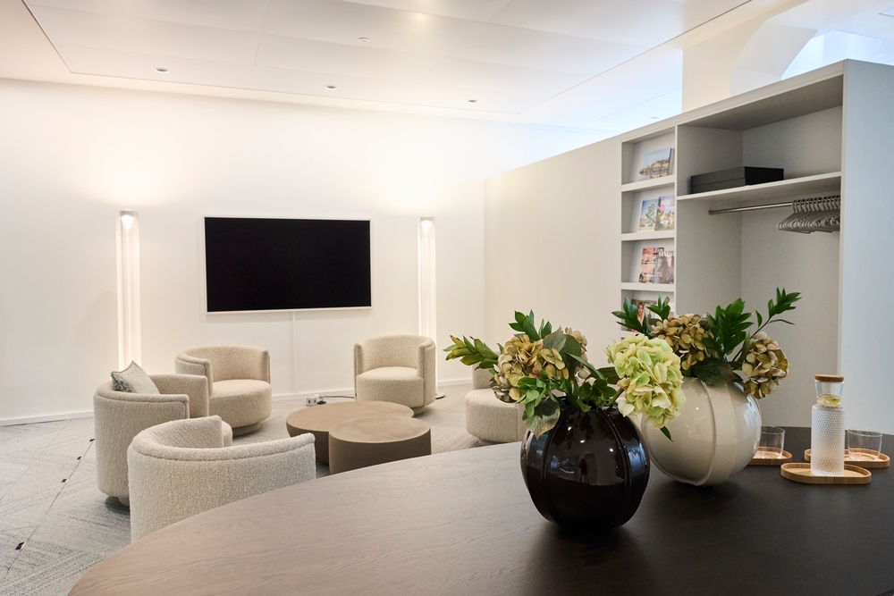 Heller Aufenthaltsbereich des Elysium Institut mit Sesseln, Bildschirm und Blumenarrangement